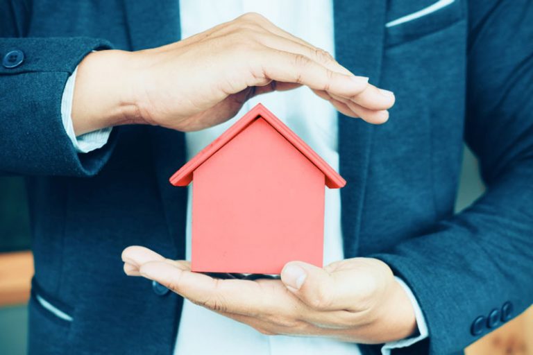 Ein Geschäftsmann hält das Model eines Einfamilienhauses in seinen Händen